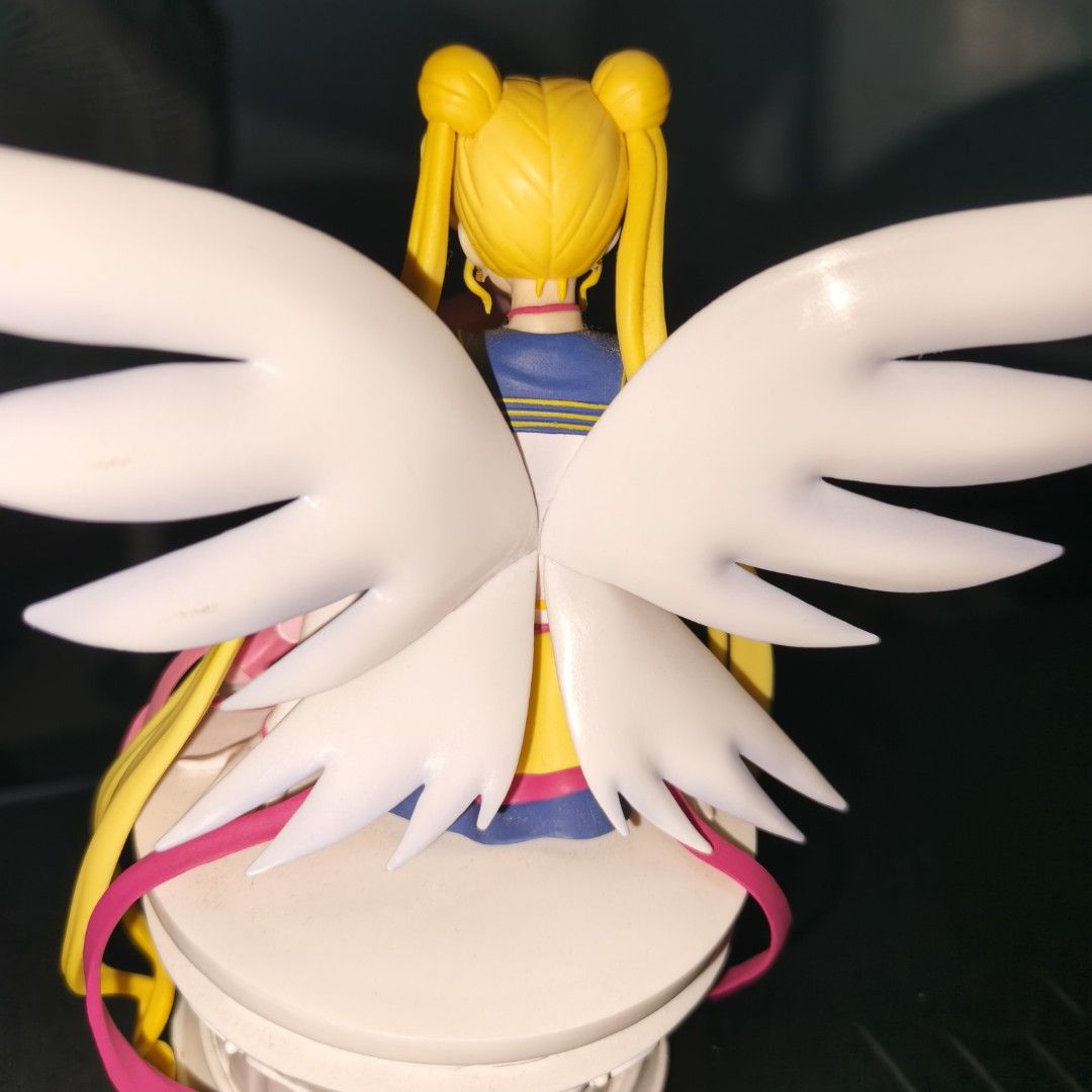 Sailor Moon and Chibi Moon Eternal (Category: Figurines & Statues) located in Plaridel. Submitted by dragonskeep (Listing ID 1402679522, Image 2). Description: - Sailor Moon and Chibi Moon figurine - Features large white wings - Perched on a white base - Made of plastic - Sailor Moon with long blonde hair and signature outfit - Chibi Moon in a pink outfit - Honest Issue: Glued Right Wing chipped during shipping from Japan. (GLUED) -Good Center pi