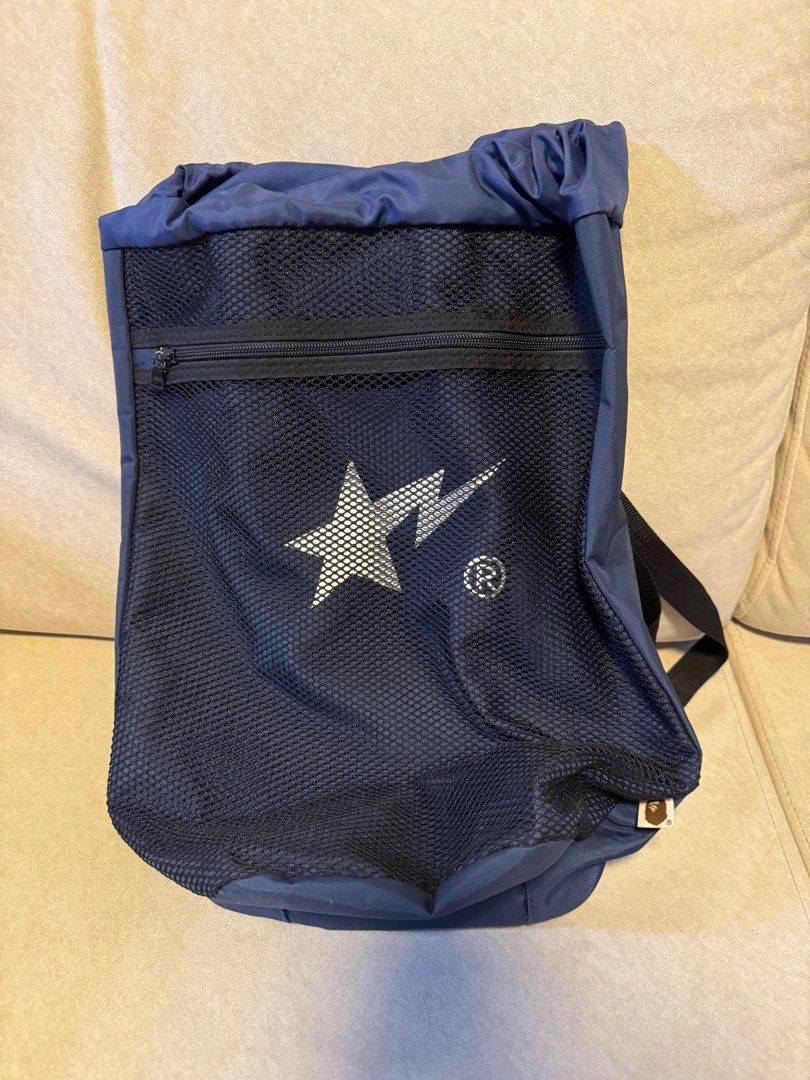 BAPE Drawstring Backpack （分類：背包）位於 Hong Kong。 由 shopaholic_2010 提交（商品編號 1407285835，圖片 2）。簡介： Navy blue drawstring backpack with a mesh front panel. Features a zippered pocket and adjustable straps. The BAPE logo is prominently displayed on the front. Includes a small tag with the BAPE logo at the bottom. The bag has a drawstring closure at the top and a small pocket inside.。