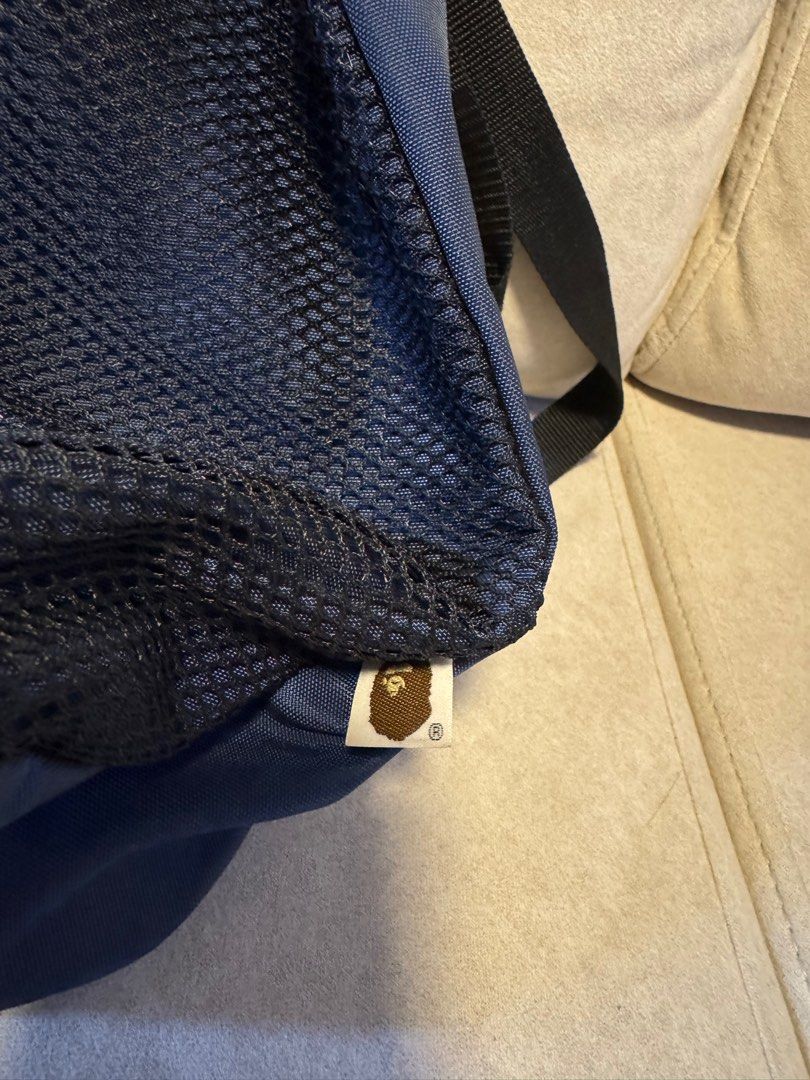 BAPE Drawstring Backpack （分類：背包）位於 Hong Kong。 由 shopaholic_2010 提交（商品編號 1407285835，圖片 3）。簡介： Navy blue drawstring backpack with a mesh front panel. Features a zippered pocket and adjustable straps. The BAPE logo is prominently displayed on the front. Includes a small tag with the BAPE logo at the bottom. The bag has a drawstring closure at the top and a small pocket inside.。