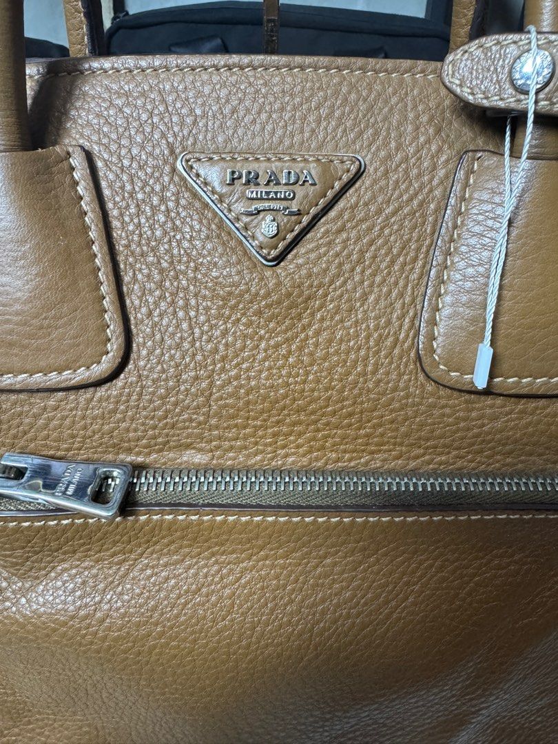 Prada Leather Tote Bag (Category: Luxury Bags & Wallets) located in Los Banos. Submitted by capsule_closet (Listing ID 1409061601, Image 2). Description: - Authentic Prada tote bag - Elegant tan color - Exterior: Front zip pocket - Main compartment: Zip closure - Interior: Prada lining and small zip pocket - Double top handles - Prada logo on front - Includes model number tag -Brought from reputable luxury bags seller.