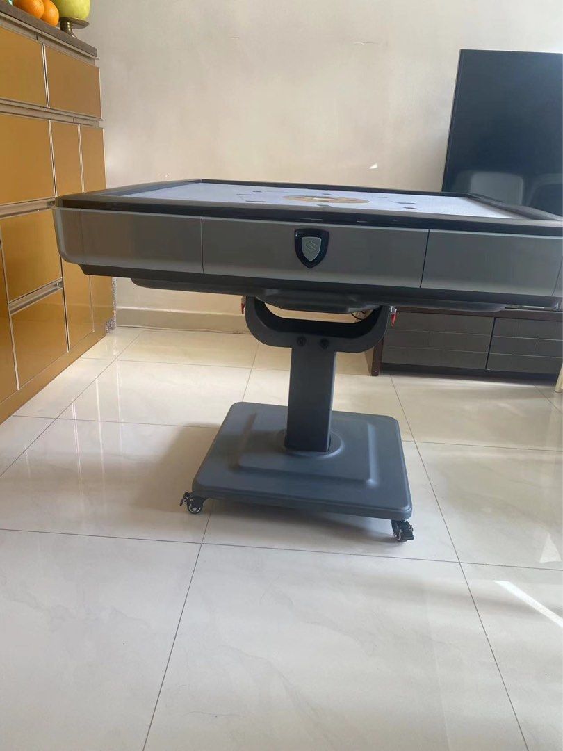 Automatic Mahjong Table （分類：互動玩具）位於 Hong Kong。 由 phrenia 提交（商品編號 1409086263，圖片 2）。簡介： Automatic mahjong table with a grey playing surface and black trim. The table has a central tile-shuffling mechanism and a built-in drawer. It is supported by a pedestal base with wheels for easy movement. Includes a set of light blue mahjong tiles. Original price $5xxx.。
