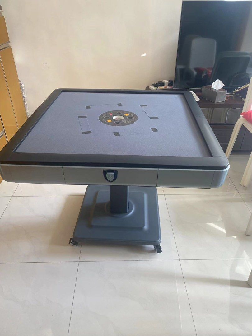 Automatic Mahjong Table （分類：互動玩具）位於 Hong Kong。 由 phrenia 提交（商品編號 1409086263，圖片 1）。簡介： Automatic mahjong table with a grey playing surface and black trim. The table has a central tile-shuffling mechanism and a built-in drawer. It is supported by a pedestal base with wheels for easy movement. Includes a set of light blue mahjong tiles. Original price $5xxx.。