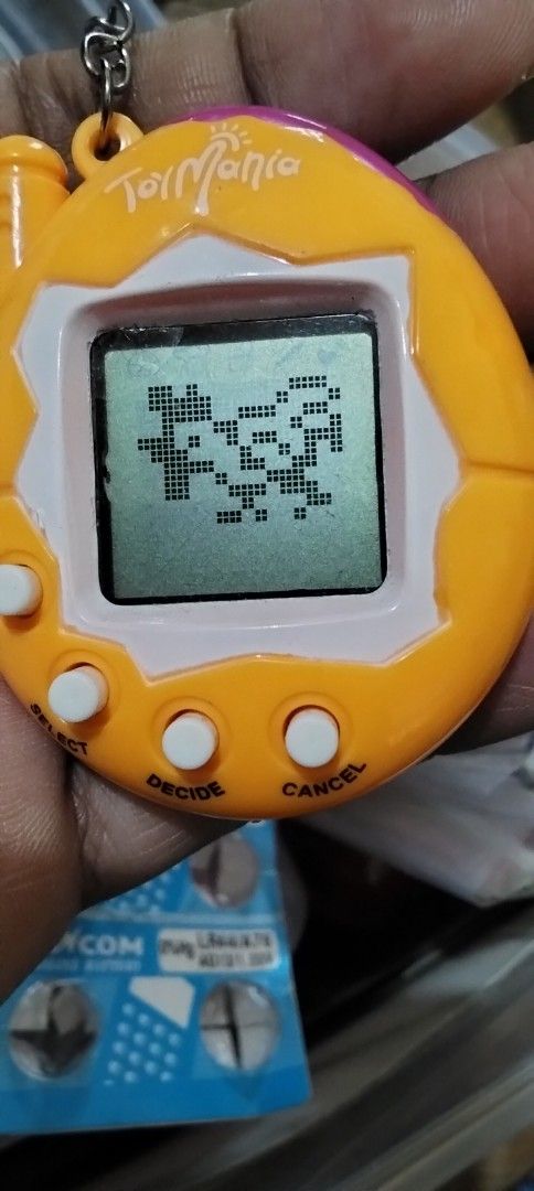 Toy Mania Virtual Pet (Category: Interactive Toys) located in Santa Rosa. Submitted by animemerchcollection (Listing ID 1409084291, Image 1). Description: - Tamagotchi Mania virtual pet - Orange and white design - Small screen and buttons - Pixelated character display - Working condition - Includes keychain attachment - Battery compartment at the back.