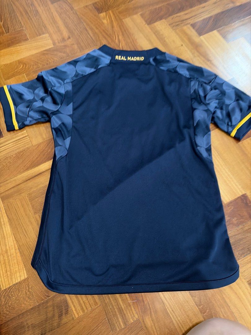 Adidas Real Madrid 2022/23 Third Jersey (Category: Babies & Kids Fashion) located in Singapore. Submitted by graceneo8024 (Listing ID 1409442817, Image 2). Description: - Official Adidas Real Madrid third jersey from the 2022/23 season. - Features the Emirates Fly Better sponsor logo. - Unique wave pattern design. - "REAL MADRID" printed on the back..
