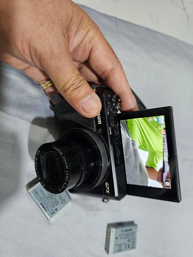 Canon PowerShot G7 X Mark II Digital Camera (Category: Cameras) located in Tagbilaran City. Submitted by lugarpogi (Listing ID 1409589463, Image 2). Description: Canon PowerShot G7 X Mark II digital camera. Includes the camera, three batteries, and a battery charger. Features a flip-up screen and a zoom lens. The camera has a strap attached. The screen displays various settings and captured images. The camera is black..