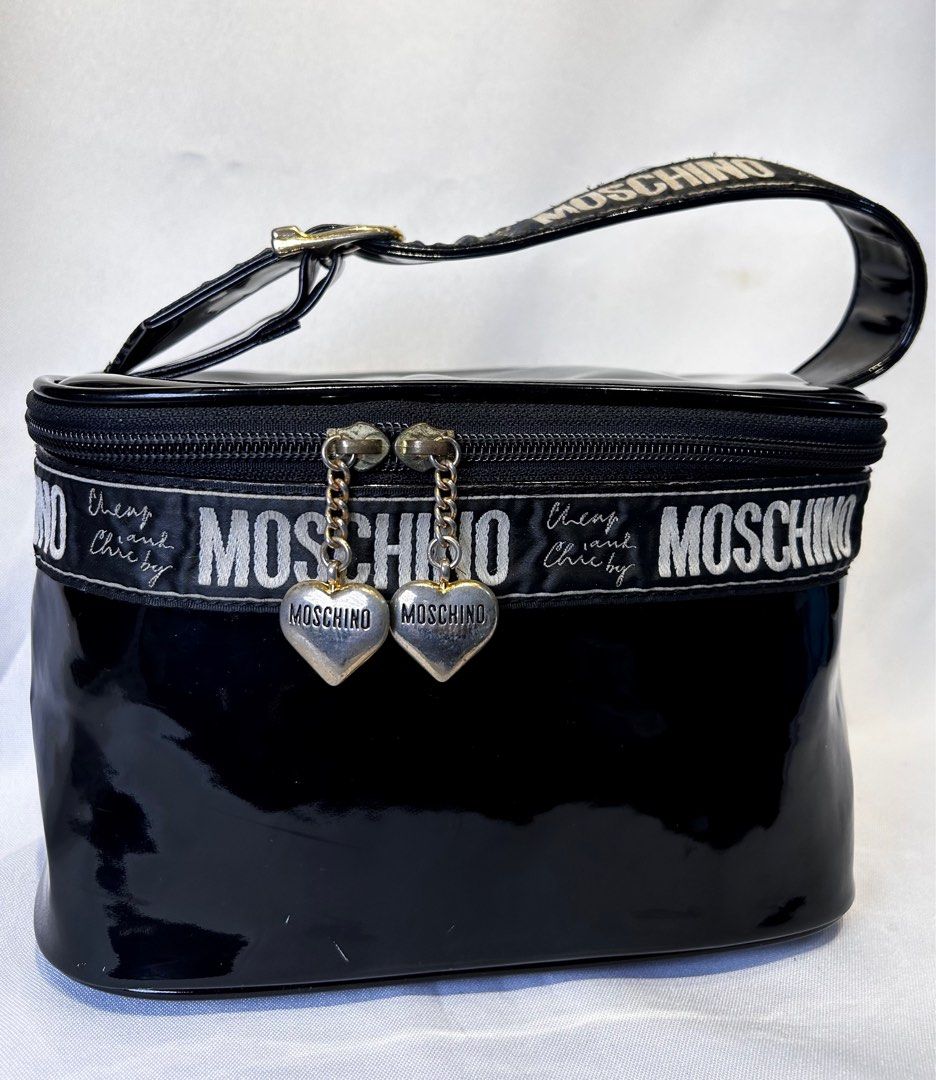 Moschino. Vanity Bag. (Category: Luxury Bags & Wallets) located in Manila. Submitted by originalvintagebagph (Listing ID 1409492746, Image 3). Description: 23 - 15 - 14 CM The bag is expensive! Black cosmetic bag by Moschino. Features a top handle and a zipper closure. The bag has a shiny exterior with the Moschino logo printed on a band around the bag. Includes a mirror inside. The interior is a gold-brown color. The bag has a heart-shaped charm