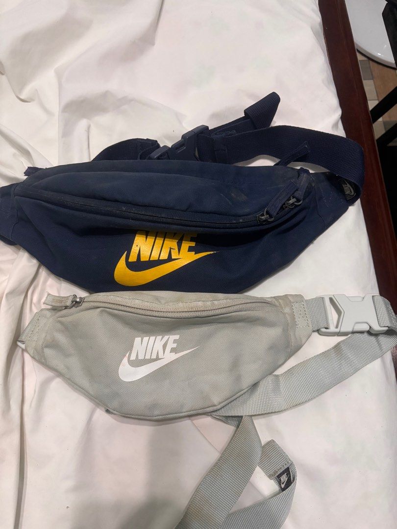 Nike Waist Bag (Category: Belt bags, Clutches and Pouches) located in Victoria. Submitted by eliphalez (Listing ID 1409613613, Image 2). Description: Two Nike waist bags are available. One is navy blue with a yellow Nike logo, and the other is light gray with a white Nike logo. Both bags have adjustable straps and a buckle closure. The navy bag shows some wear and tear. The gray bag also shows some stains. For mens and womens Both for 600pesos.