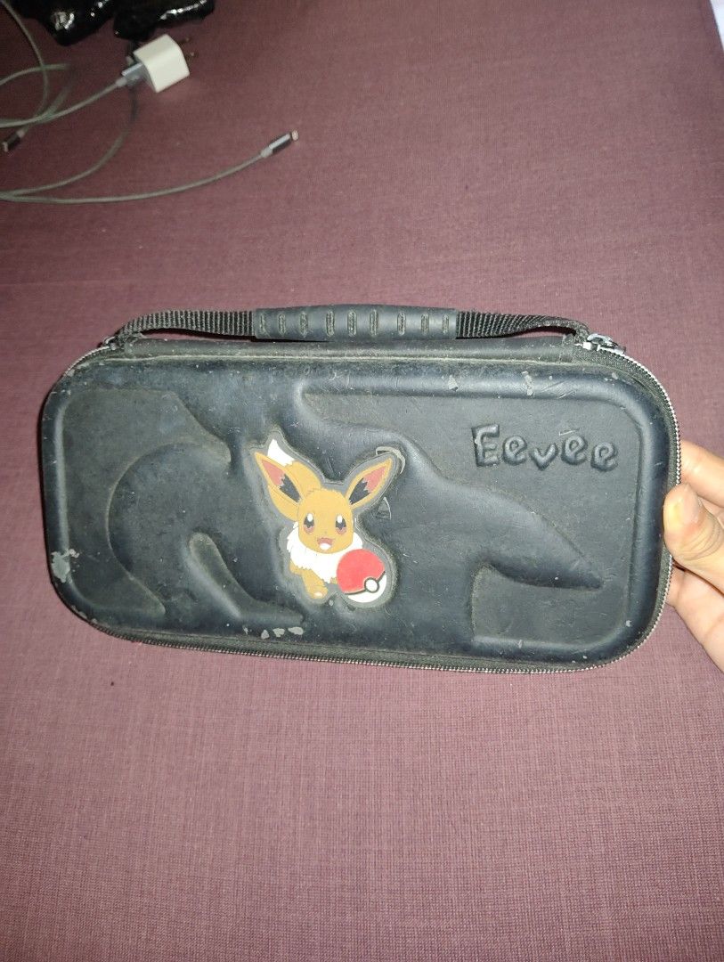 Pokemon Eevee Nintendo Switch Case (Category: Nintendo) located in Pasig City. Submitted by hazelscollectibles (Listing ID 1409468467, Image 1). Description: - Black Switch case see. pic for deets - Features an adorable Eevee design - Includes a convenient handle - Secure zipper closure - Internal slots for game cartridges - Mesh pocket for accessories - Designed to hold your Switch console and accessories.