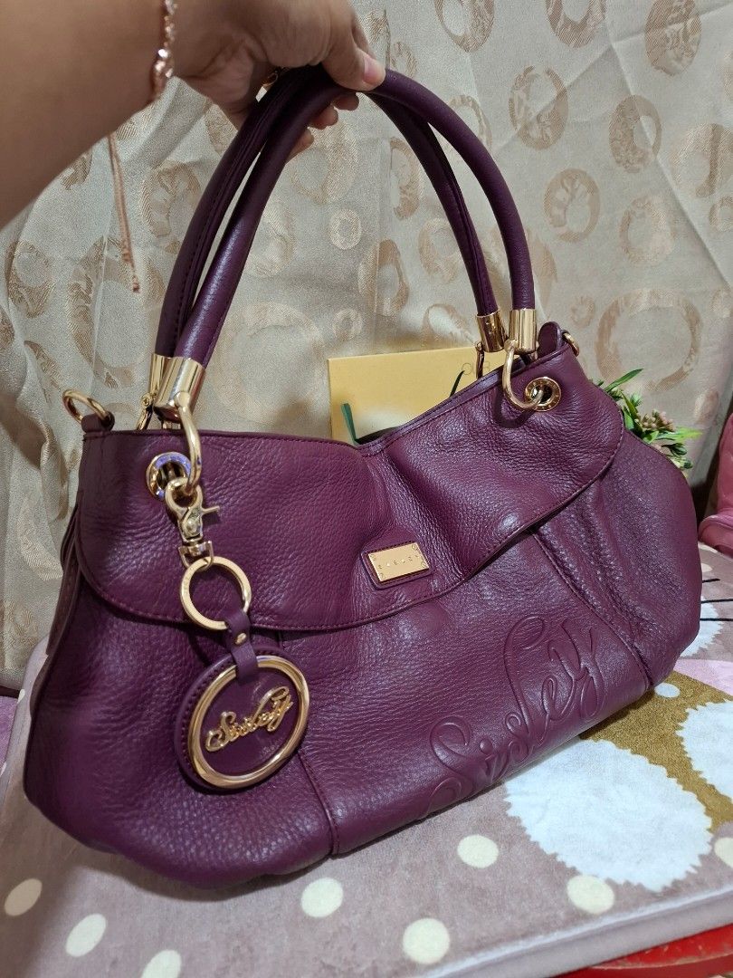 SISLEY Handbag - Purple [ORIGINAL] (Category: Luxury Bags & Wallets) located in Rizal. Submitted by she_prelovedbagsfromkorea (Listing ID 1409540831, Image 1). Description: - Authentic Sisley handbag - Stunning purple color - Elegant gold-tone hardware - Versatile top handle and detachable shoulder strap - Convenient interior zip pocket - Includes a stylish Sisley charm - Luxurious textured finish - Secure gold zipper - Interior lined with a patt