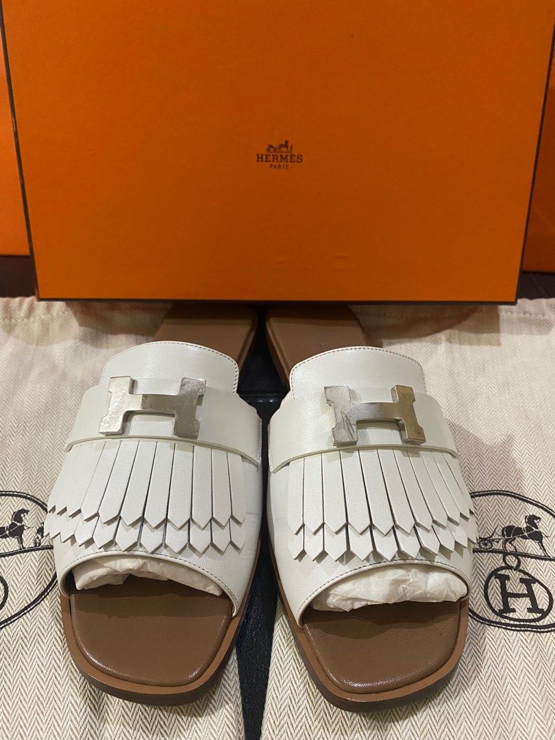 Hermes Oran Sandals White (Category: Sneakers & Footwear) located in Las Pinas. Submitted by abluxebrands (Listing ID 1409907265, Image 1). Description: - Authentic Hermes Oran sandals - Color: White - Iconic H buckle and fringe detailing - Brown leather sole - Includes original box and dust bag - Hermes logo embossed on insole - Size: Not specified.