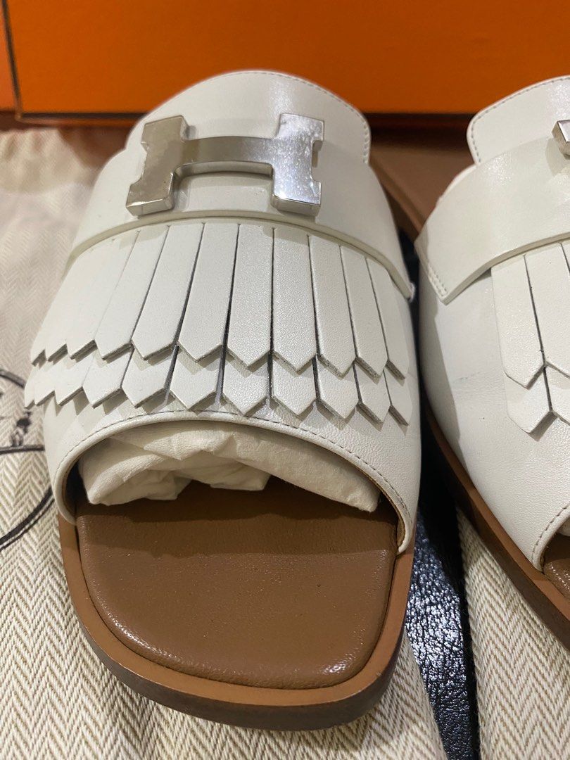 Hermes Oran Sandals White (Category: Sneakers & Footwear) located in Las Pinas. Submitted by abluxebrands (Listing ID 1409907265, Image 2). Description: - Authentic Hermes Oran sandals - Color: White - Iconic H buckle and fringe detailing - Brown leather sole - Includes original box and dust bag - Hermes logo embossed on insole - Size: Not specified.