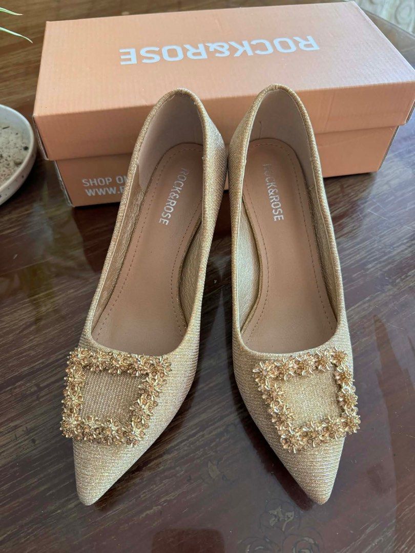 Rock & Rose Venus Heels - Size 36 (Category: Heels) located in Cavite. Submitted by hardt0get (Listing ID 1409859643, Image 2). Description: Elegant Rock & Rose Venus heels in size 36. Features a gold glittery finish with a decorative buckle. Comes with the original box. The heels have a pointed toe and a small heel. The soles are black. The box shows the original price of ₱999.00..