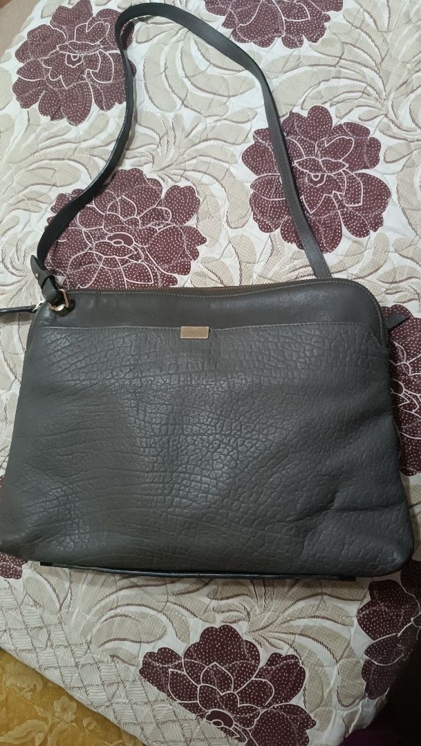 Bruno Magli Shoulder Bag (Category: Luxury Bags & Wallets) located in La Trinidad. Submitted by leezhine (Listing ID 1410152152, Image 1). Description: -Stylish Bruno Magli shoulder bag in a greyish color. - Features a textured genuine leather exterior with a top zipper closure. -The bag has a shoulder strap and a gold-toned metal accent with the brand name. -The interior is lined with a patterned fabric and includes multiple compartments for org