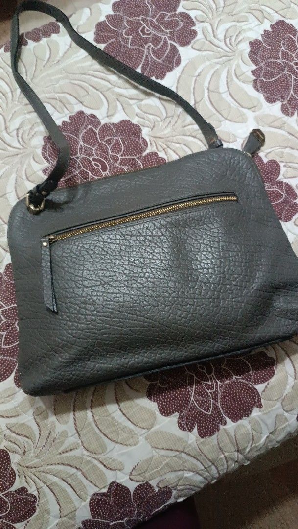Bruno Magli Shoulder Bag (Category: Luxury Bags & Wallets) located in La Trinidad. Submitted by leezhine (Listing ID 1410152152, Image 2). Description: -Stylish Bruno Magli shoulder bag in a greyish color. - Features a textured genuine leather exterior with a top zipper closure. -The bag has a shoulder strap and a gold-toned metal accent with the brand name. -The interior is lined with a patterned fabric and includes multiple compartments for org