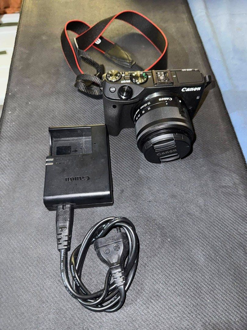 Canon EOS M3 Mirrorless Camera with Lens (Category: Cameras) located in Pateros City. Submitted by goodthift (Listing ID 1410232416, Image 1). Description: - Canon EOS M3 mirrorless camera (black body) - Includes lens - Charger and power cable included - Red and black camera strap - Lens cap included - Screen visible in images.