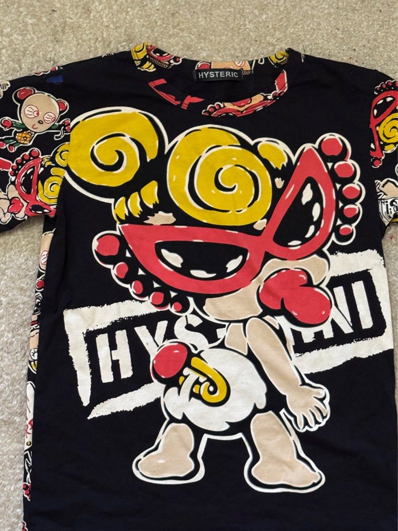 Hysteric Glamour Graphic Tee (Category: Tshirts & Polo Shirts ) located in Paranaque City. Submitted by passion_pluto (Listing ID 1410419726, Image 2). Description: - Black Hysteric Glamour graphic tee - Features a unique cartoon character design - Design includes a character with yellow hair and a red mask - Short sleeves and a classic crew neck - Sleeves adorned with cartoon character pattern - Brand name prominently displayed on the collar.