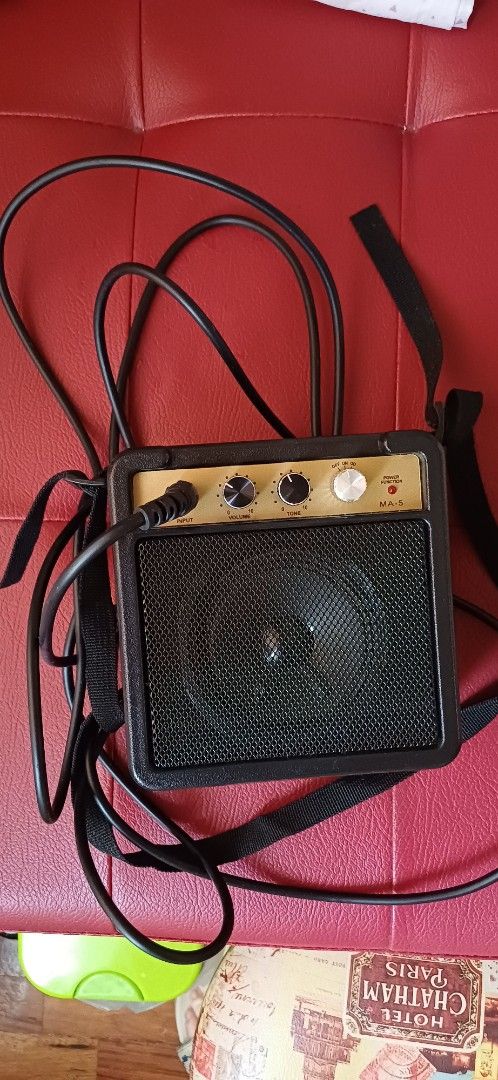 Mini Guitar Amplifier (Category: Musical Instruments) located in Manila. Submitted by kahlen36985 (Listing ID 1407429042, Image 2). Description: Compact mini guitar amplifier with a built-in speaker. Features volume, tone, and gain controls. Includes a strap for easy portability. The amplifier has a black speaker grill and a gold-colored control panel. Comes with free cable.