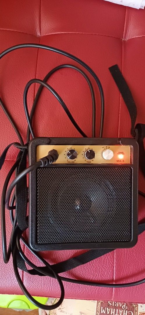 Mini Guitar Amplifier (Category: Musical Instruments) located in Manila. Submitted by kahlen36985 (Listing ID 1407429042, Image 1). Description: Compact mini guitar amplifier with a built-in speaker. Features volume, tone, and gain controls. Includes a strap for easy portability. The amplifier has a black speaker grill and a gold-colored control panel. Comes with free cable.