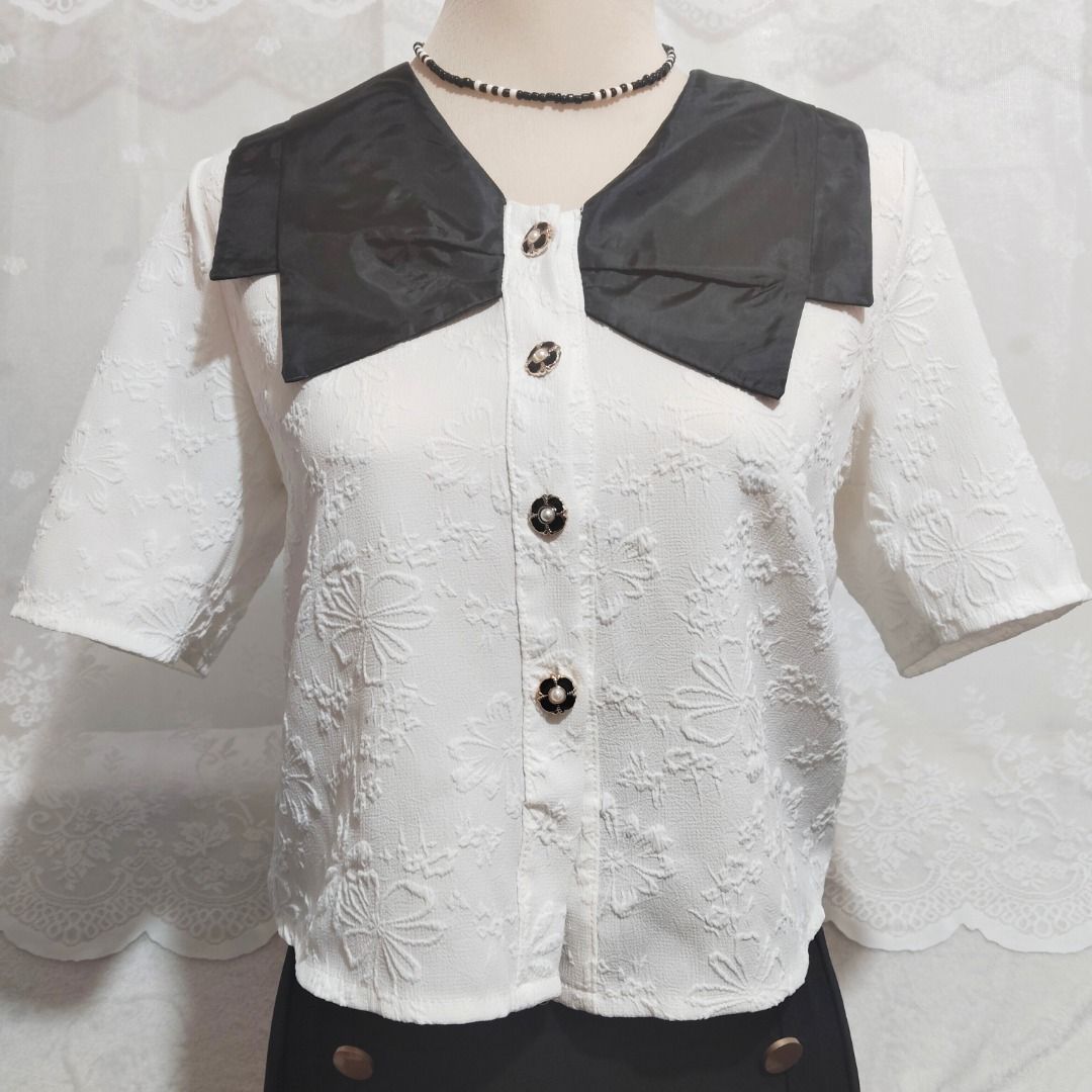 White Floral Button Down Blouse with Black Ribbon Collar (Category: Blouses) located in Mandaluyong City. Submitted by princesspockets (Listing ID 1410851329, Image 3). Description: The ribbon-style collar is so cute! The fabric has embossed flower details all over, and the flower-shaped buttons are working and in perfect condition. So many cute details in such a simple top! Best fit: M-SL 🌸 FLAT LAY MEASUREMENTS 🌸 Bust: 36-37 in Length: 20 in 