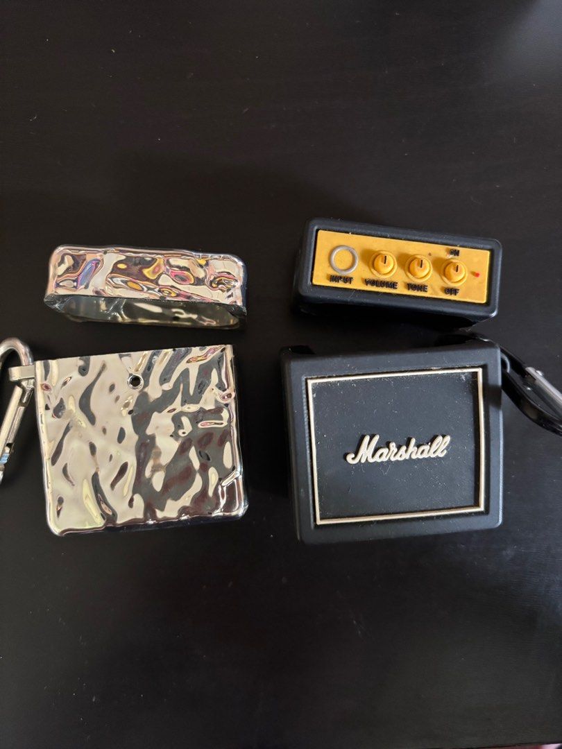 AirPods 2 Cases (2 for PHP200) (Category: Earphones) located in Valenzuela. Submitted by popyard (Listing ID 1410933233, Image 1). Description: PHP200.00 for both cases! - Unique AirPods cases available: - Marshall amplifier design: Black with gold knobs and logo. - Silver case: Textured, metallic finish. - Both cases include a carabiner clip. - Designed to protect your AirPods..