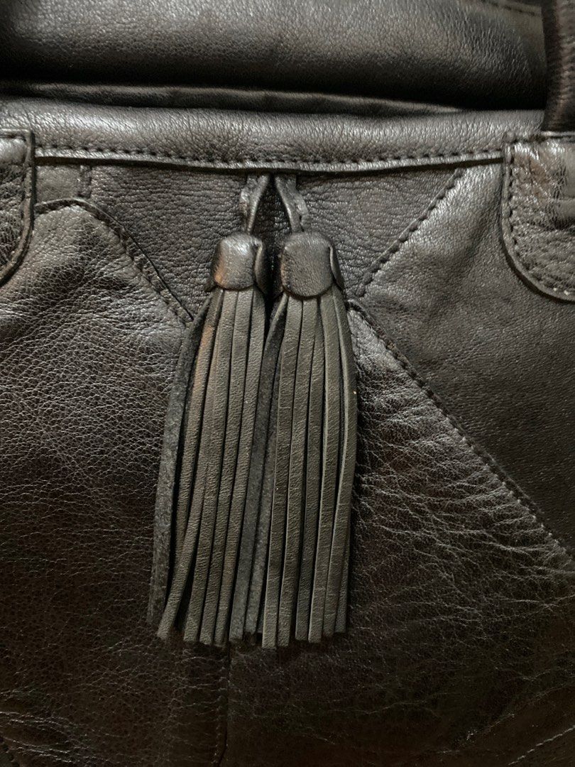 Ibiza Genuine Leather Tote Bag (Category: Tote Bags) located in Quezon City. Submitted by modificabagsph (Listing ID 1410950990, Image 2). Description: Black leather tote bag from Ibiza. Features a zip closure, dual top handles, and decorative tassels. Includes an interior zip pocket and multiple compartments. The bag has a patch design and a metal Ibiza logo. The interior lining is black. The bag has a tag with the Ibiza logo..