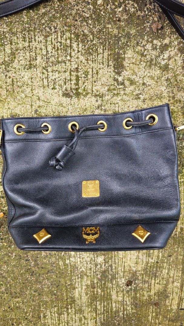 MCM Black Shoulder Bag (Category: Luxury Bags & Wallets) located in Kibawe. Submitted by Thrift_ni_Babac (Listing ID 1411185493, Image 2). Description: - Authentic MCM shoulder bag - Black with gold-tone hardware - Drawstring and zip closures - Shoulder strap - Interior MCM logo - Exterior with minor wear and tear - Gold-tone MCM logo on front - Unique design with gold accents Issue: Please refer to last 3 photos.