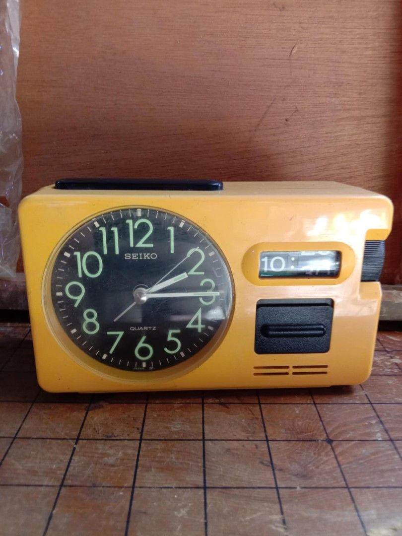 Seiko Quartz Alarm Clock (Category: Clocks) located in Quezon City. Submitted by jpnvintageonline (Listing ID 1411296509, Image 1). Description: - Vintage Seiko alarm clock - Retro orange color - Black clock face with luminous hands and numerals - Digital time display - Alarm and snooze function - Rectangular shape with handle - Working condition.