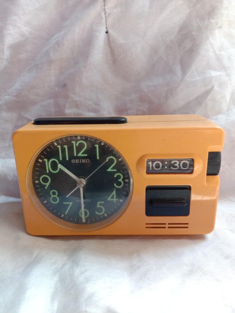 Seiko Quartz Alarm Clock (Category: Clocks) located in Quezon City. Submitted by jpnvintageonline (Listing ID 1411296509, Image 2). Description: - Vintage Seiko alarm clock - Retro orange color - Black clock face with luminous hands and numerals - Digital time display - Alarm and snooze function - Rectangular shape with handle - Working condition.