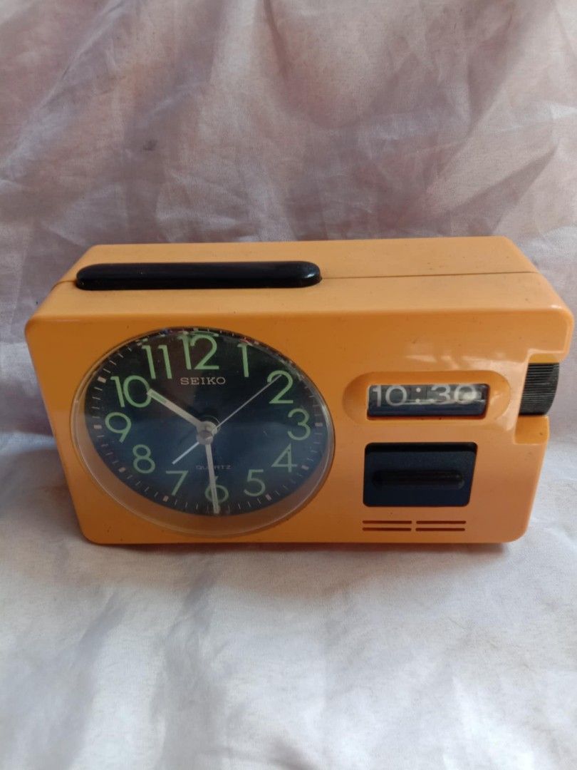 Seiko Quartz Alarm Clock (Category: Clocks) located in Quezon City. Submitted by jpnvintageonline (Listing ID 1411296509, Image 3). Description: - Vintage Seiko alarm clock - Retro orange color - Black clock face with luminous hands and numerals - Digital time display - Alarm and snooze function - Rectangular shape with handle - Working condition.