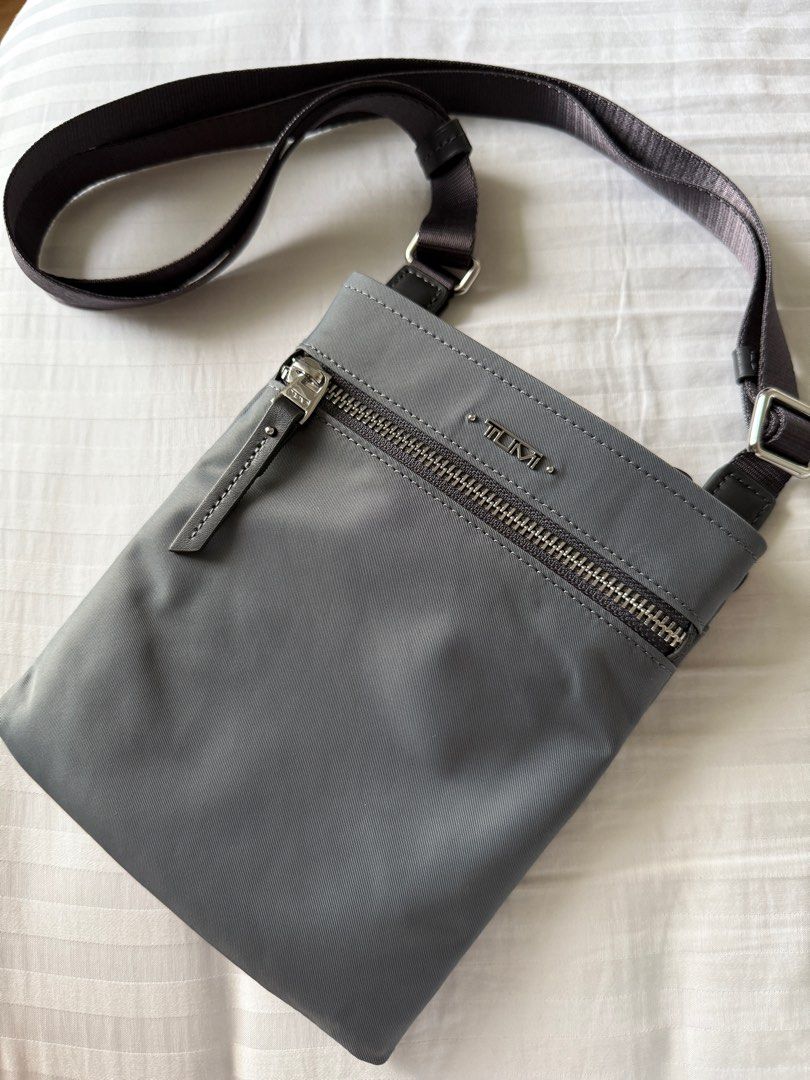 Tumi Cassandra mini pocket bag (Category: Cross-body Bags) located in Pasig City. Submitted by abbyrds (Listing ID 1411348788, Image 1). Description: Tumi Cassandra mini pocket bag features a sleek, gray design with a zippered main compartment and an adjustable strap. The bag includes a front zippered pocket and a Tumi logo on the front with a back pocket with magnetic closure. The interior reveals a fabric lining with a Tumi label and 3 card slo