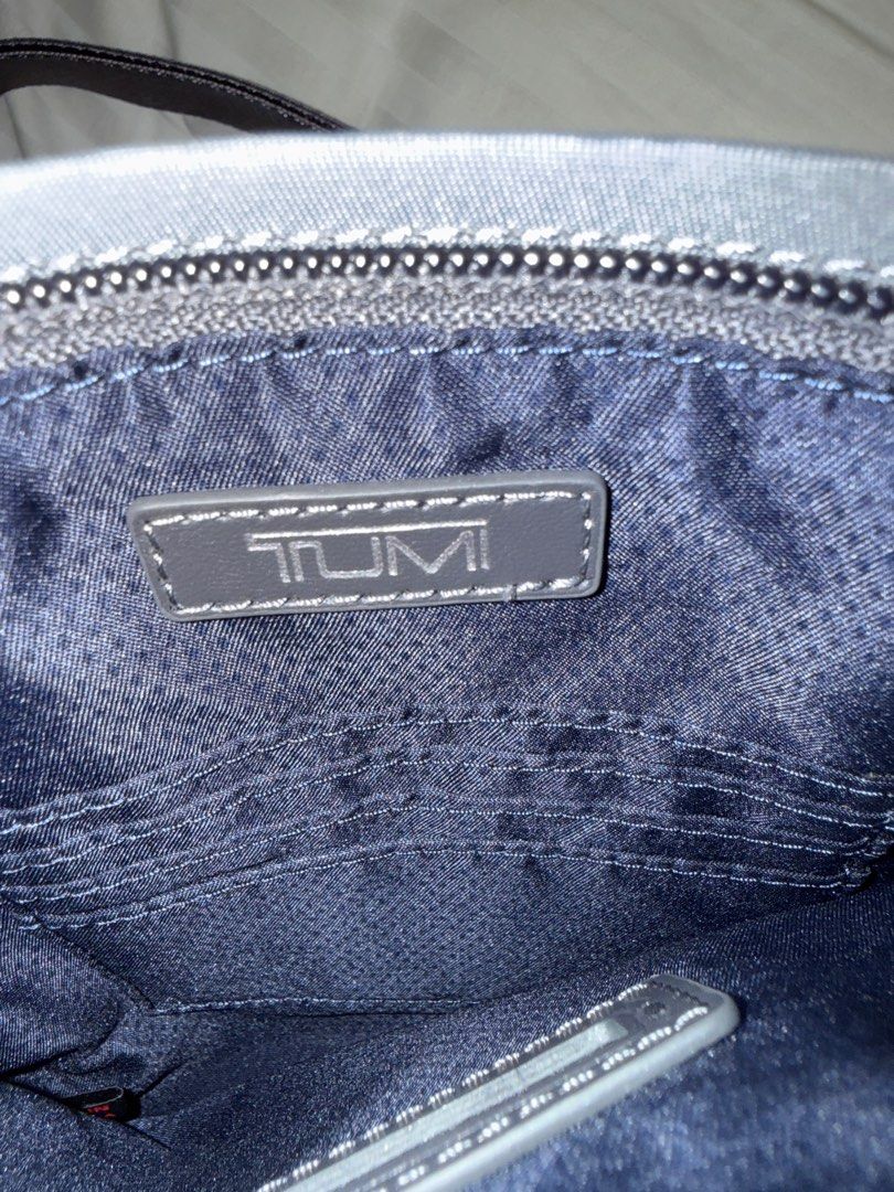 Tumi Cassandra mini pocket bag (Category: Cross-body Bags) located in Pasig City. Submitted by abbyrds (Listing ID 1411348788, Image 3). Description: Tumi Cassandra mini pocket bag features a sleek, gray design with a zippered main compartment and an adjustable strap. The bag includes a front zippered pocket and a Tumi logo on the front with a back pocket with magnetic closure. The interior reveals a fabric lining with a Tumi label and 3 card slo