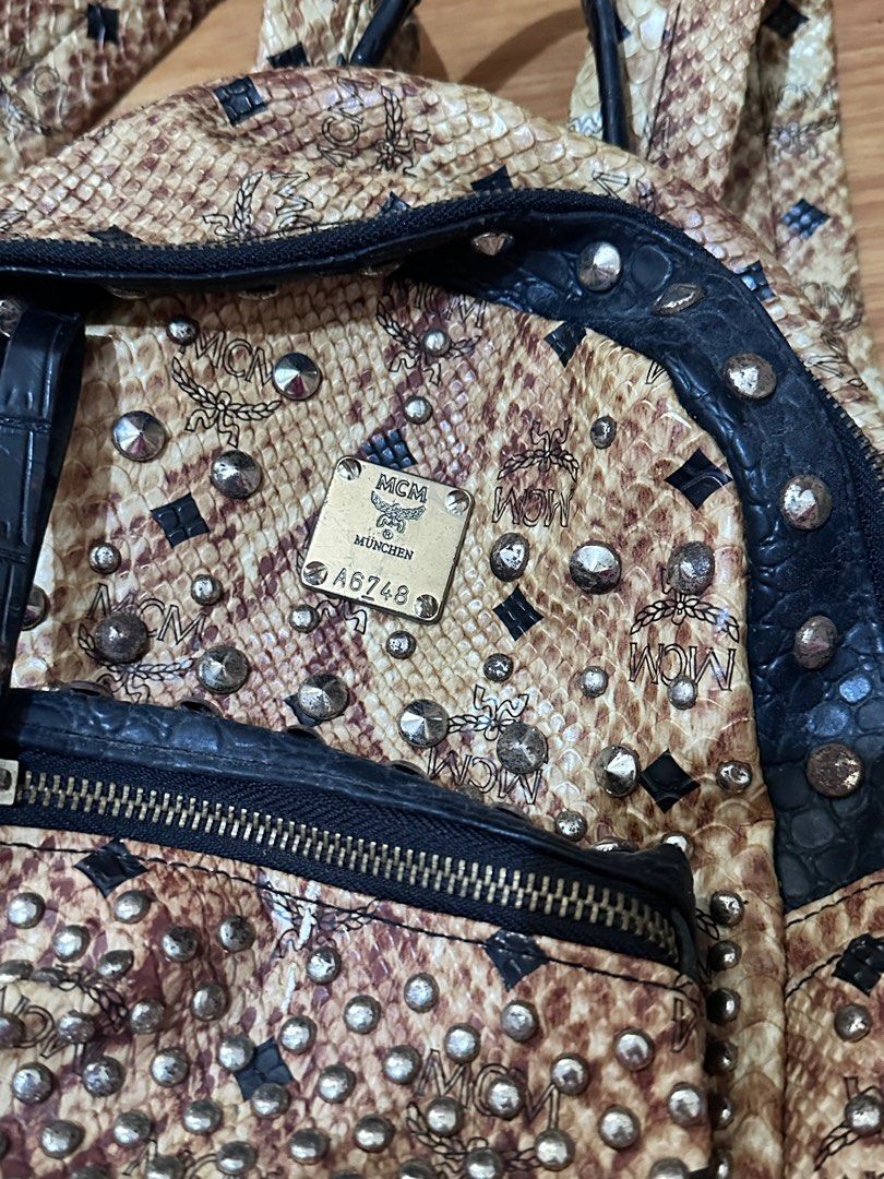 MCM Studded Backpack (Category: Luxury Bags & Wallets) located in Batangas. Submitted by prelovedby.juu (Listing ID 1411840357, Image 3). Description: - MCM backpack (authenticity not guaranteed: gifted item) - Snakeskin pattern with studded detailing - Front pocket with zipper closure - Top handle - Black interior with multiple compartments - Adjustable straps - MCM logo visible on front and back.