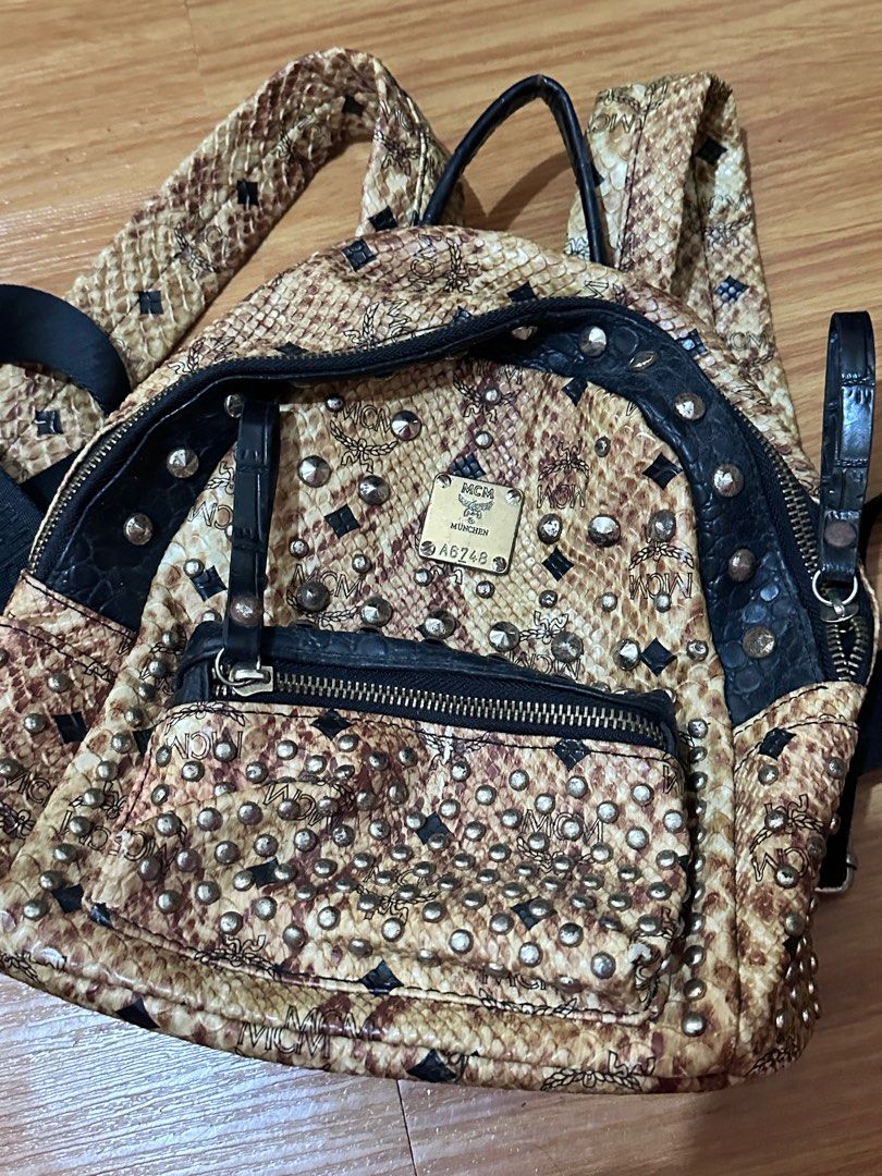 MCM Studded Backpack (Category: Luxury Bags & Wallets) located in Batangas. Submitted by prelovedby.juu (Listing ID 1411840357, Image 2). Description: - MCM backpack (authenticity not guaranteed: gifted item) - Snakeskin pattern with studded detailing - Front pocket with zipper closure - Top handle - Black interior with multiple compartments - Adjustable straps - MCM logo visible on front and back.
