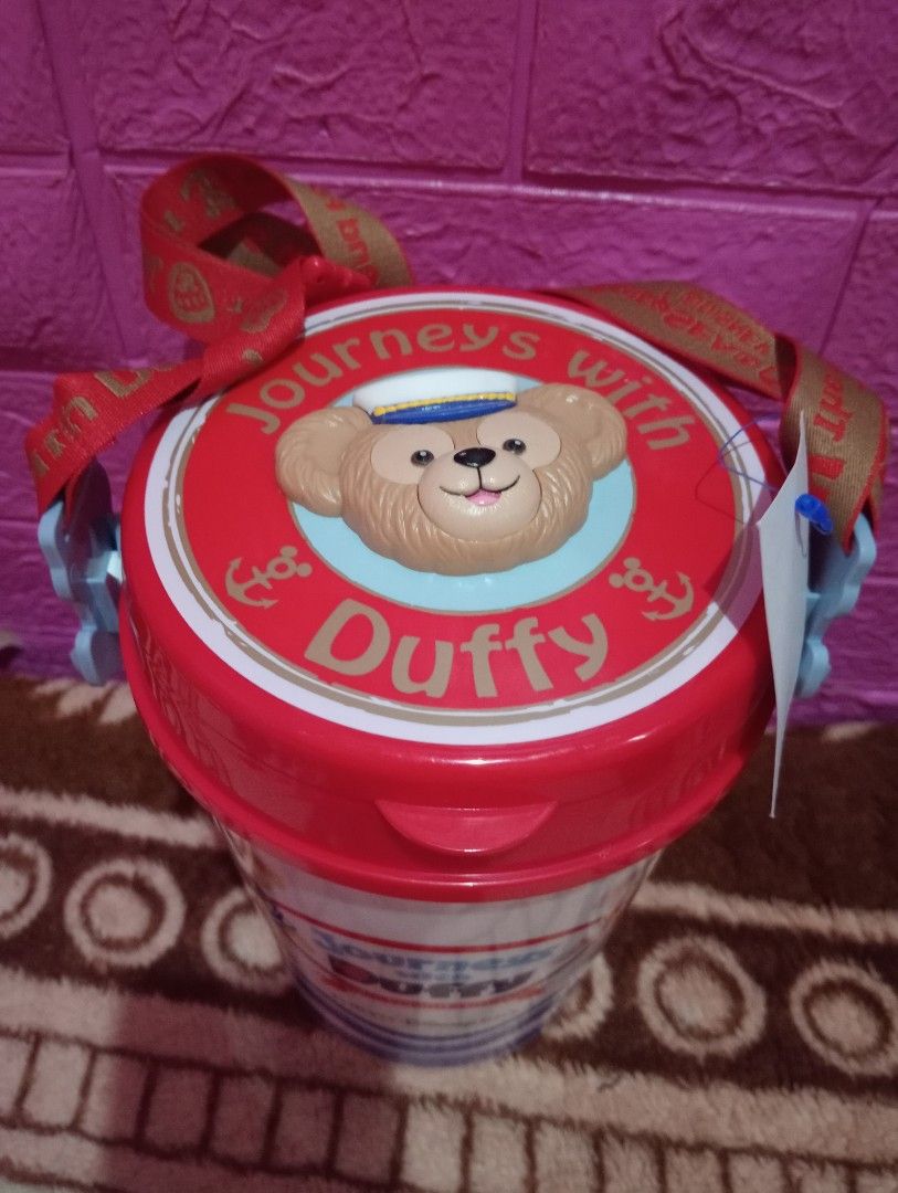 Duffy Journeys pop corn bucket (Category: Water Bottles & Tumblers) located in Bulacan. Submitted by renasophiatoystore2020 (Listing ID 1412215381, Image 2). Description: Tumbler features Duffy from Tokyo DisneySea's "Journeys with Duffy" collection. It has a red lid with a Duffy design and a matching strap. The tumbler is white with blue accents and Duffy graphics. It includes a tag with a price of ¥110. The tumbler is designed to keep your drin