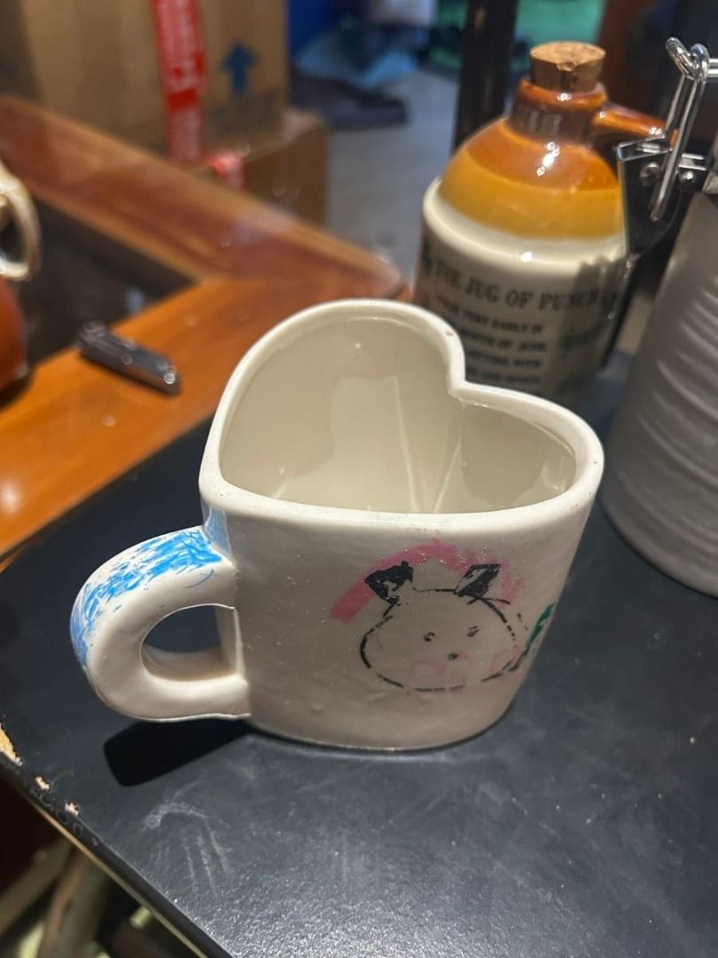 Handmade Heart-Shaped Ceramic Mug (Category: Coffee & Tea Tableware) located in General Mariano Alvarez. Submitted by kapitbahayfinds (Listing ID 1412310260, Image 2). Description: Handmade Heart-Shaped Ceramic Mug 📝 Description: Handmade heart-shaped ceramic mug featuring an off-white glaze with a hand-painted black and pink animal face design. The handle is decorated with an abstract blue and white pattern, and the slightly irregular form high