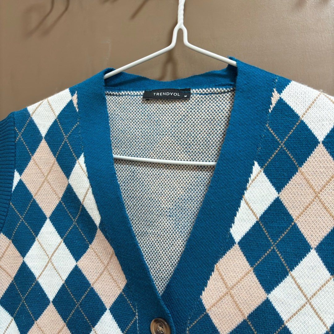 Trendyol Zalora Argyle Knit Vest Medium (Category: Sleeveless) located in Balanga. Submitted by heyyletsdeclutter (Listing ID 1412201115, Image 2). Description: - Trendyol argyle knit vest from Zalora - Classic argyle pattern in teal, beige, and white - V-neck design - Button closures - Cropped length - Sleeveless - Knit material for a comfortable fit - Perfect for layering.