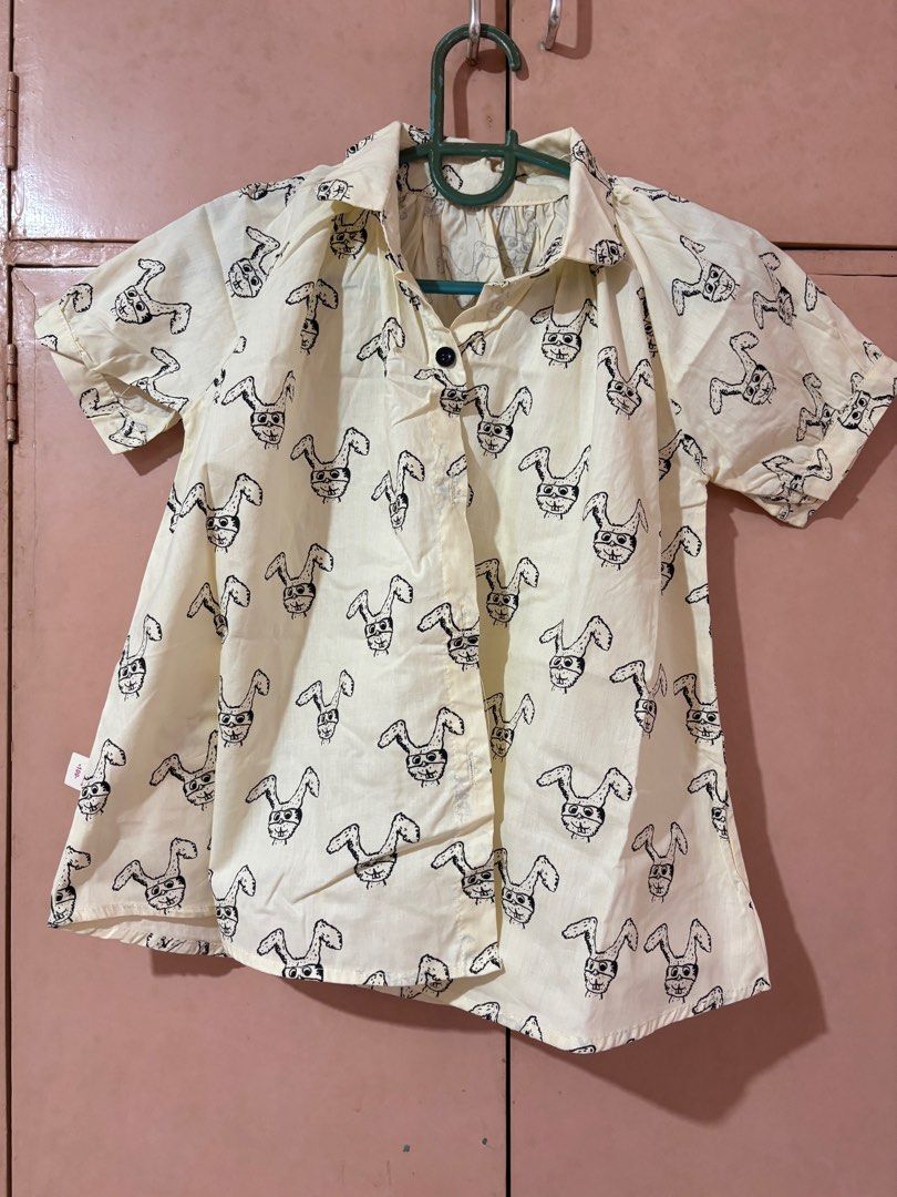 Kids Bunny Print Shirt (Category: Shirts) located in San Mateo. Submitted by angelthings.cute (Listing ID 1412407500, Image 1). Description: - Adorable kids shirt - Features a fun bunny print - Short sleeves and collared neckline - Light cream color - Black bunny graphics all over - Size: 100 - Measurements: 16 inches across the chest, 17 inches in length.