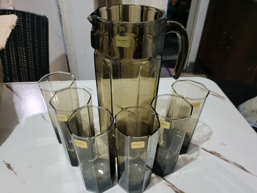 Vintage Pitcher and Glass Set (Category: Pitchers & Dispensers) located in Quezon City. Submitted by 09275375503 (Listing ID 1412486290, Image 1). Description: Luminarc pitchel Set includes a pitcher and six glasses. The glasses have a unique geometric design. The set is a smoky brown color. The pitcher has a handle for easy pouring. Each glass has a sticker on it. This set is perfect for serving drinks at home..