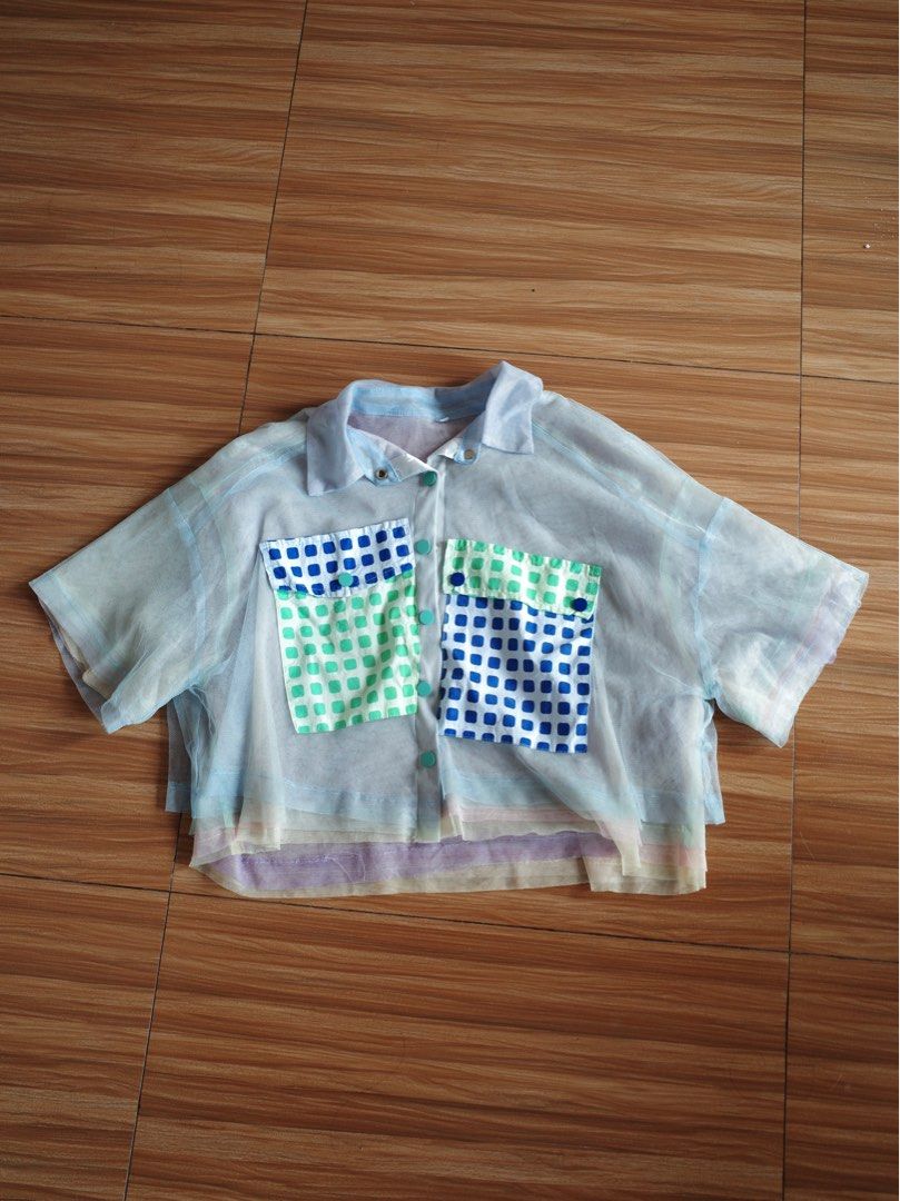 Sheer Cropped Top with Pocket Details (Category: Blouses) located in Makati City. Submitted by bluelocker (Listing ID 1407653392, Image 1). Description: - Sheer cropped top - Collared neckline - Short sleeves - Button-down closure - Two front pockets with blue and green square pattern - Layered hem design - Primarily light blue color with pastel accents.