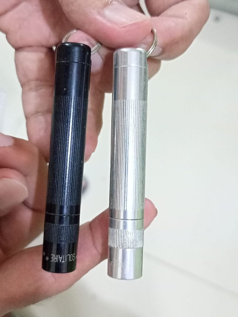 Flashlight Maglite Mini (Category: Lighting) located in Caloocan City. Submitted by 2nddesignf33843 (Listing ID 1407883169, Image 3). Description: Listing includes two Mag Instrument Solitaire flashlights. One is black, and the other is silver. Both flashlights have a textured grip and a small keyring attachment. The black flashlight is marked "MAG INSTRUMENT" and "MADE IN USA". The silver flashlight is marked "SOLITAIRE". Php 600 for the pair. U