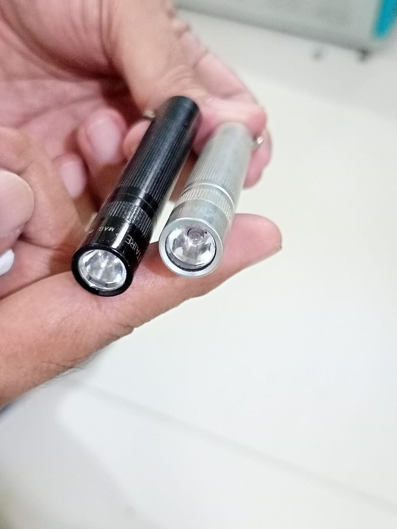 Flashlight Maglite Mini (Category: Lighting) located in Caloocan City. Submitted by 2nddesignf33843 (Listing ID 1407883169, Image 1). Description: Listing includes two Mag Instrument Solitaire flashlights. One is black, and the other is silver. Both flashlights have a textured grip and a small keyring attachment. The black flashlight is marked "MAG INSTRUMENT" and "MADE IN USA". The silver flashlight is marked "SOLITAIRE". Php 600 for the pair. U