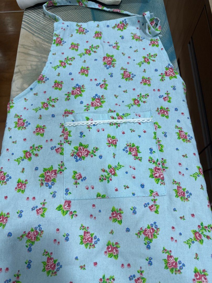 Floral Print Apron with Pocket (Category: Coats, Jackets and Outerwear) located in Quezon City. Submitted by struddels (Listing ID 1407899386, Image 1). Description: - Floral print apron - Pink, blue, and green floral design on light blue background - Features a pocket with white lace trim - Adjustable neck and waist straps - Ideal for cooking and baking - Adds a vintage touch to your kitchen.