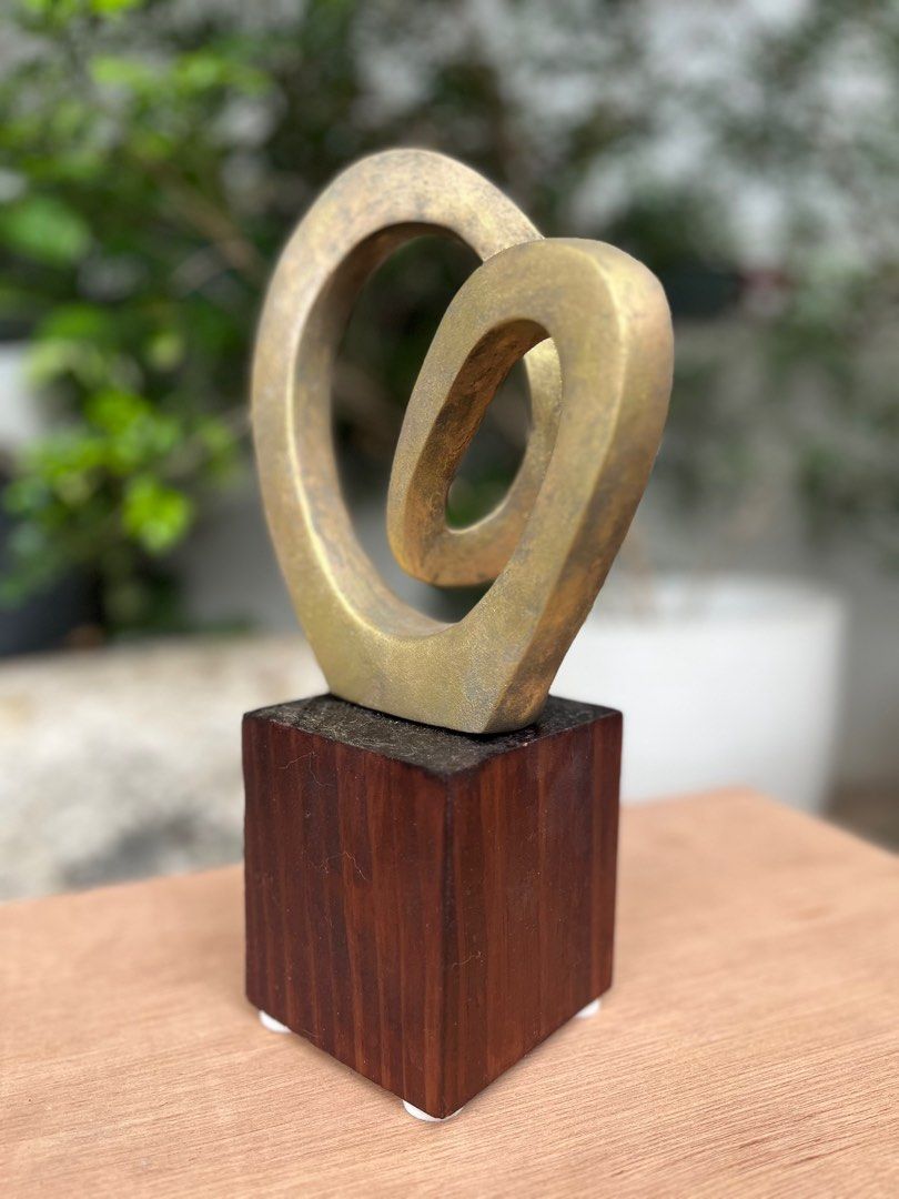 Abstract allum Sculpture on Wooden Base (Category: Other Home Decor) located in Pasig City. Submitted by wilsonwill38327 (Listing ID 1408319121, Image 1). Description: - Gold-toned abstract sculpture - Looping design - Mounted on a dark wooden, square-shaped base - Adds visual interest - Great for desks and shelves Medium: Solid Aluminum Size: 4x6x 15 inches including base Finish: rustic btonze/ gold Year: 2025 Artist: Wilson William Includes sig