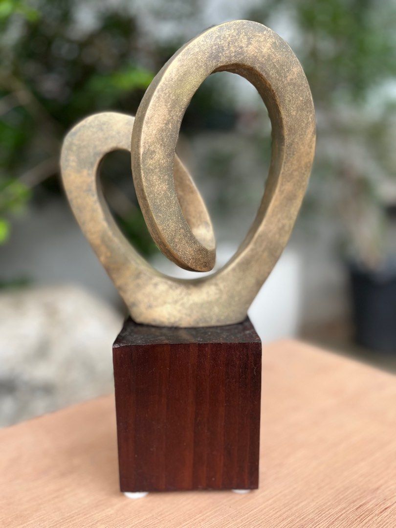 Abstract allum Sculpture on Wooden Base (Category: Other Home Decor) located in Pasig City. Submitted by wilsonwill38327 (Listing ID 1408319121, Image 2). Description: - Gold-toned abstract sculpture - Looping design - Mounted on a dark wooden, square-shaped base - Adds visual interest - Great for desks and shelves Medium: Solid Aluminum Size: 4x6x 15 inches including base Finish: rustic btonze/ gold Year: 2025 Artist: Wilson William Includes sig