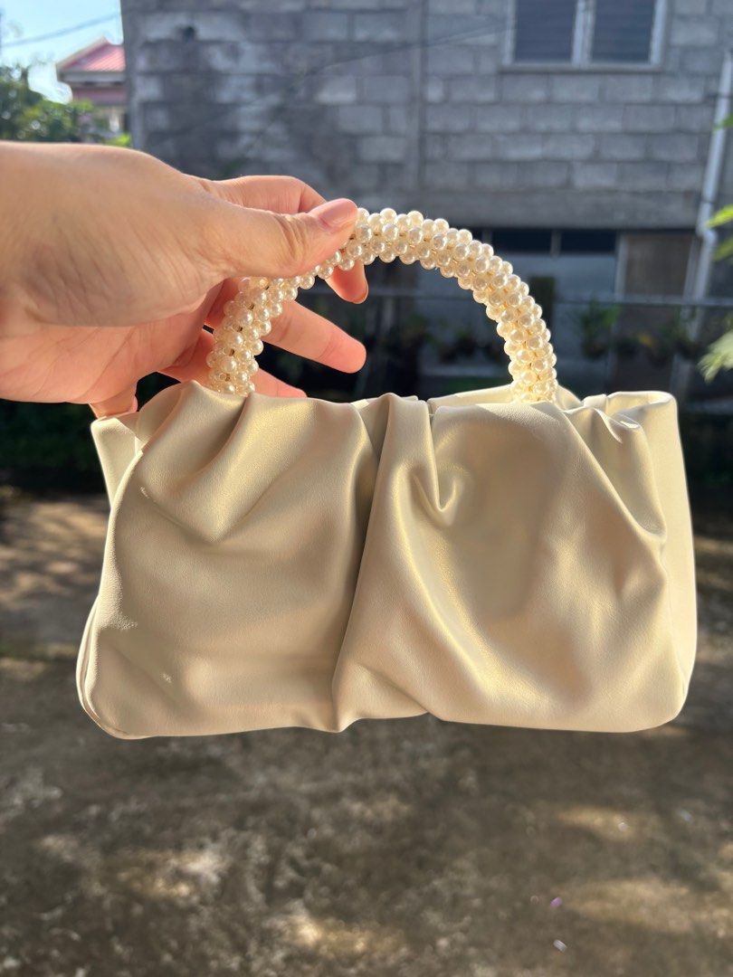 Cream-colored Handbag with Pearl Handle (Category: Luxury Bags & Wallets) located in Clarin. Submitted by declutter_station101 (Listing ID 1408495975, Image 1). Description: - Cream-colored handbag - Unique pearl-beaded handle - Gathered design - Smooth, possibly leather-like material - Gold-colored hardware - Perfect for any occasion.