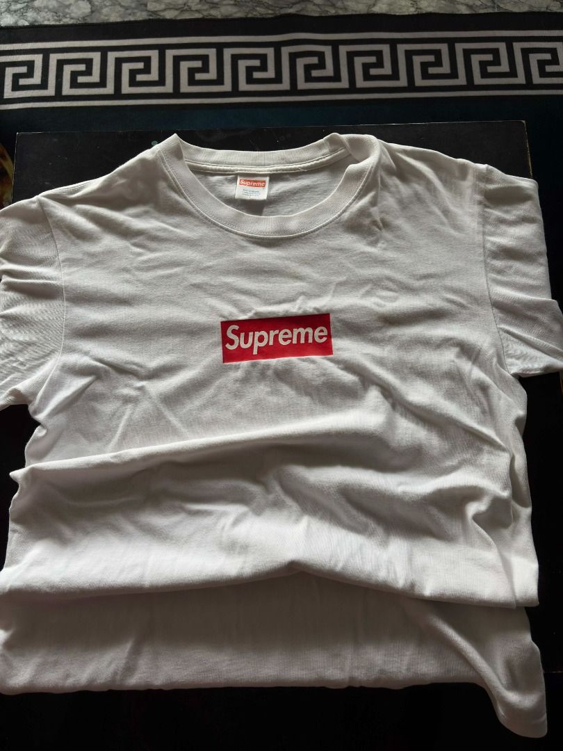 ( Authentic ) Supreme iconic box logo tee (Category: Tshirts & Polo Shirts ) located in Quezon City. Submitted by mr.mclovin (Listing ID 1408539489, Image 1). Description: White Supreme Box Logo T-shirt. Features the iconic red box logo on the chest. The tag is visible at the neckline. The shirt is folded..