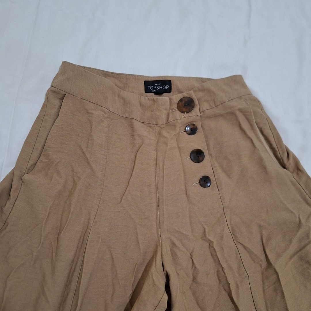 Topshop Petite Wide Leg Pants (Category: Other Bottoms) located in Pasig City. Submitted by avcan (Listing ID 1408661015, Image 2). Description: Stylish Topshop Petite wide-leg pants in a versatile tan color. Features a button closure and two front pockets. The pants are a size UK6 and made in Vietnam. The waist measures approximately 14 inches across, when laid flat. Length is about 30.5 inches. .
