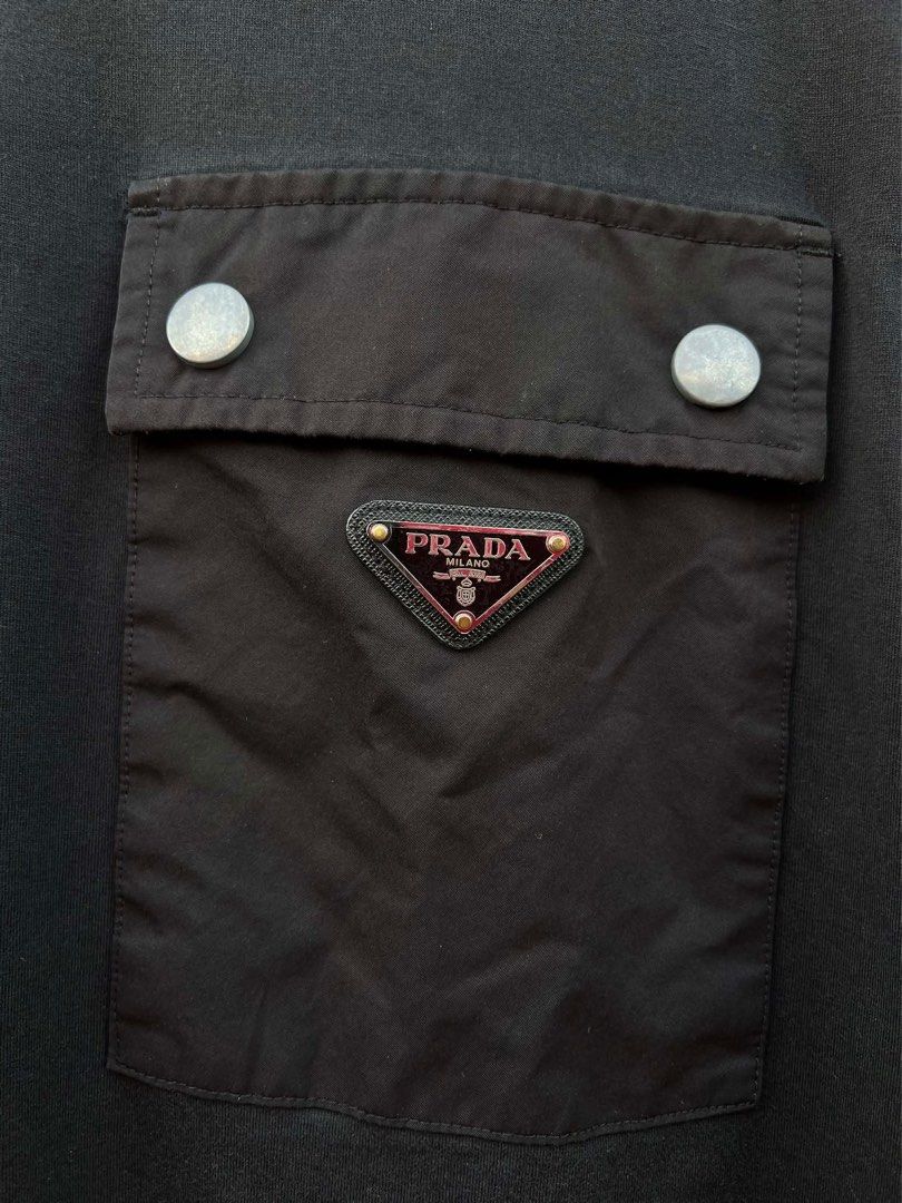 Prada Black Pocket T-shirt (Category: Luxury Apparel) located in Bacolod City. Submitted by novymaesel14868 (Listing ID 1408700556, Image 2). Description: - Prada black t-shirt - Chest pocket with Prada logo - Silver button closure on pocket - Crew neck and short sleeves - Made in Indonesia - Fabric: 100% cotton Size XL Dimes 22x28 Excellent Condition DM to Purchase 📩.