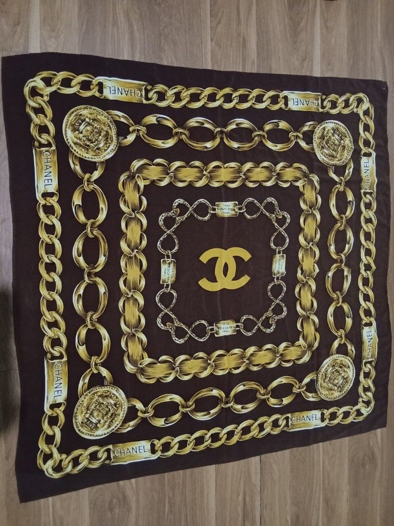 Chanel silk scarf (Category: Scarves) located in Bulacan. Submitted by nifftyythrifty (Listing ID 1361462580, Image 2). Description: The image shows a vintage Chanel silk scarf from the 1990s. It features a brown background with gold chain links and the iconic CC logo. Material: 100% silk Design: Gold chain links, CC logo, and "CHANEL" text Era: Circa 1990 Size: Approximately 90cm x 90cm Origin: Made in France Style: Vintage, classic Care: Dry cl