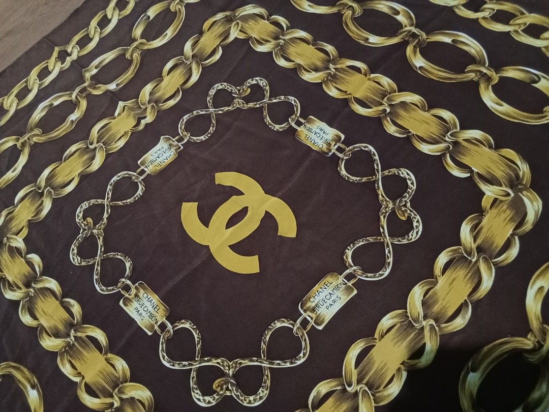 Chanel silk scarf (Category: Scarves) located in Bulacan. Submitted by nifftyythrifty (Listing ID 1361462580, Image 3). Description: The image shows a vintage Chanel silk scarf from the 1990s. It features a brown background with gold chain links and the iconic CC logo. Material: 100% silk Design: Gold chain links, CC logo, and "CHANEL" text Era: Circa 1990 Size: Approximately 90cm x 90cm Origin: Made in France Style: Vintage, classic Care: Dry cl